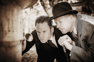 Sherlock Holmes und Dr. Watson begutachten mit einer Lupe etwas.