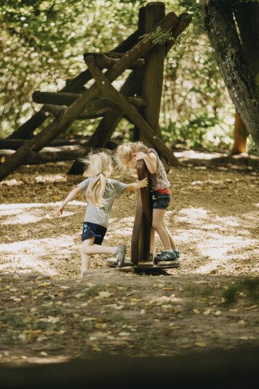 Ein Mädchen gibt einem anderen Mädchen Schwung auf einem Karrussell auf dem Waldspielplatz.
