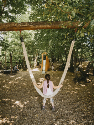Ein Mädchen sitzt auf einem dicken Seil, das als Schaukel an einem Baum befestigt ist.